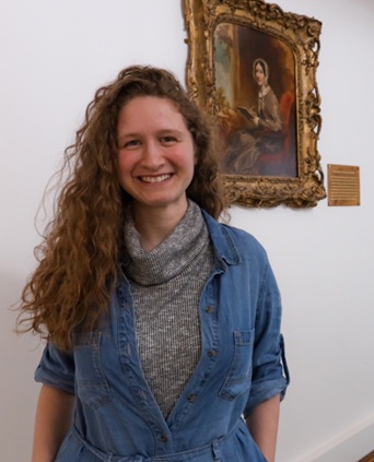 woman with curly hair stood in front of a portrait of Mary Somerville